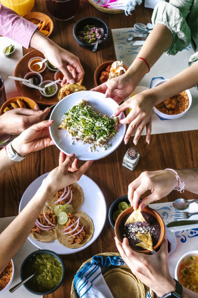 A picture of hand all reaching towards the center of a table, all sharing dinner together.