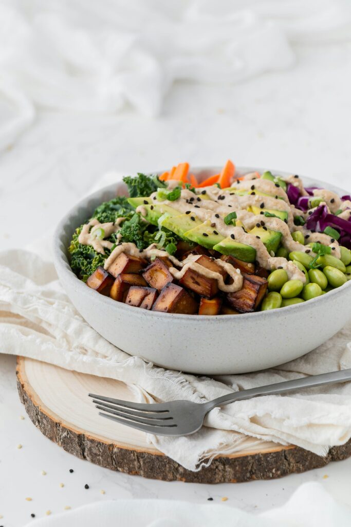 A picture of a bowl with tofu, avocado, kale, edamame, carrots, and purple cabbage.